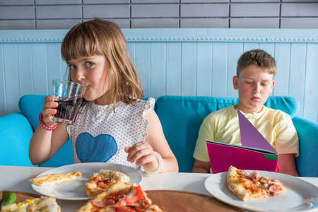 Children eat in a cafe eat Italian pizza and drink cola.の写真素材