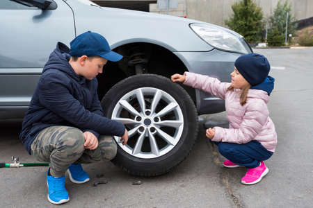 Children at the broken car, looking at the wheel. Car repair services.の写真素材