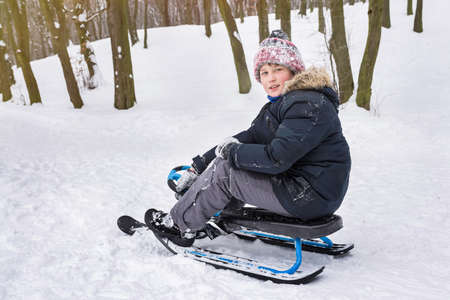 A boy rides a snow scooter outdoors in winter. Winter vacation and holidays.の写真素材