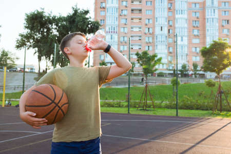 A teenager drinks water on a basketball court. Healthy lifestyle and sport concepts.