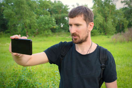 A young man is recording a video blog in the park on the phone.
