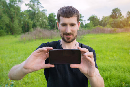A young man in the park takes pictures on the phone and blogs on social networks.