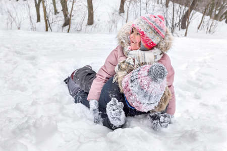 A girl in the snow is playing with her brother in a park in a winter day.の写真素材