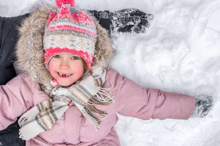 A portrait of a little girl lying in the snow.の写真素材