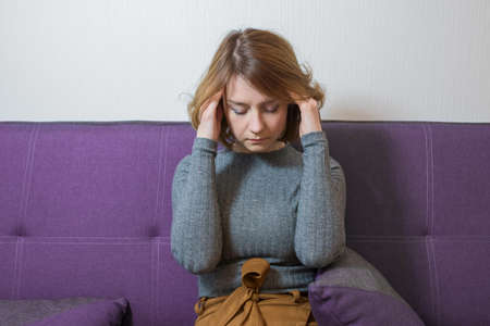 Young woman with a headache sitting on the couch, in the office of a psychologist doctor.の写真素材