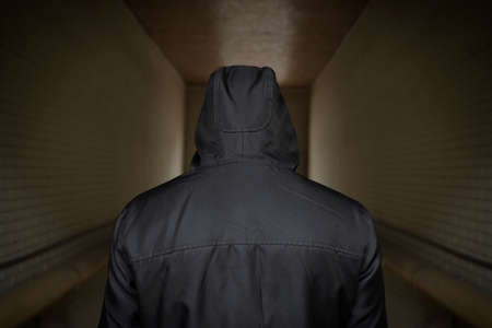 A man in a hood on the street. Social problems, drug addiction and criminal activity. The view from the back.の写真素材