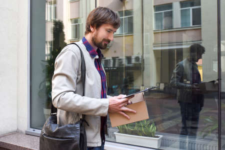 A bearded man with documents in his hands, against the backdrop of a modern building in the background. The concept of business failures and the problem of unemployment, laid off, crisis.の写真素材