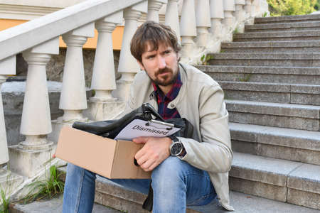 A depressed man who has lost his job sits on the steps near a building alone. Crisis, fired from work. Social problem of unemployment, Economic crisis.の写真素材
