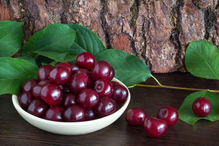 Fresh cherries in a dish on wooden table. cherry tree branch, sweet cherriesの写真素材