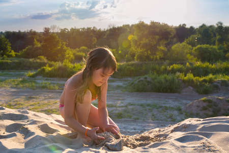 Little girl on the beach making a sand castle at sunset.の写真素材