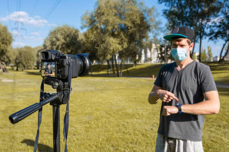 A male blogger in a protective mask looks at the camera and talks on a city street. Video recording, social media, lifestyleの写真素材