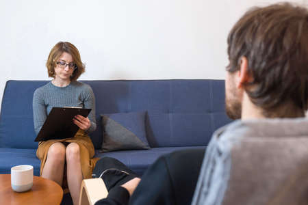 Female psychologist takes notes during a session of psychological therapy. A man with problems came to a consultation with his doctor. Mental health concept.の写真素材