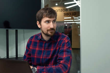 Portrait of a young man sitting at a table in the office and working on a computer. Co-working, business. Business and entrepreneurship conceptの写真素材
