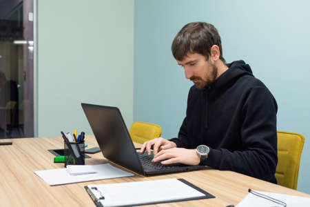 Young man working on a laptop sitting at his workplace in the office. Consulting, training, co-working, business concept.の写真素材