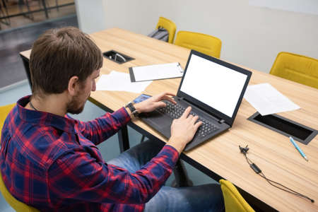 A young man sits in an office and works on a desktop computer. Business concept. Side view.の写真素材