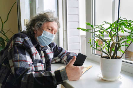 An elderly man in a protective mask on self-isolation speaks by phone via video link.の写真素材