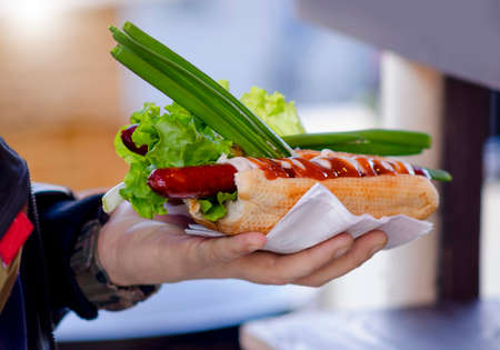 Hot dogs with tomato, pickles, onions in a hand on the street.の写真素材