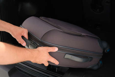 Male hands take luggage out of the trunk of a car. Vacation, travel concept.