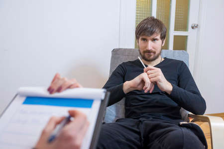 A man at a psychotherapist, sitting in a chair, talks about his problems. Healthcare concept of a professional psychologist doctor.の写真素材