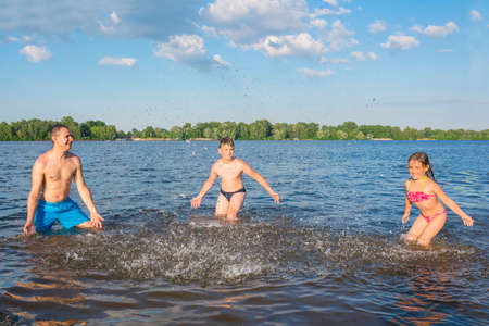 Father and two children playing on the beach in the water. Happy family on vacation. Summer vacation conceptの写真素材
