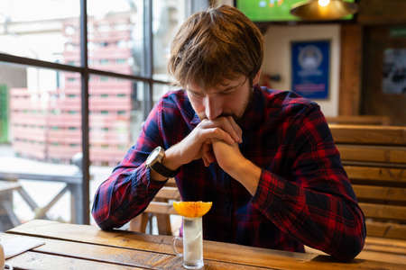 A drunk man at a bar, sitting alone at a table. Fight against alcohol addiction, crisis, unemployment, loneliness, depressionの写真素材