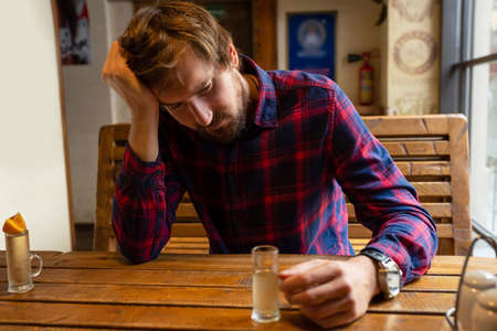A young man in a bar is struggling with alcohol addiction. The concept of alcoholism, crisis, unemployment, loneliness, depressionの写真素材
