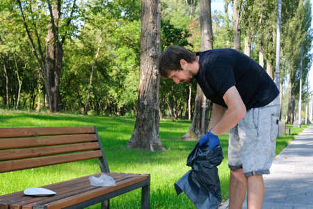 Volunteer man with trash bag collects rubbish in a public park. Garbage collection, environmental problemsの写真素材