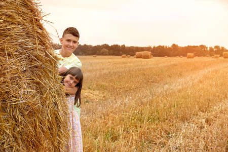 Children play in the field behind a haystack and pose for the camera. Children in nature. Lifestyleの写真素材