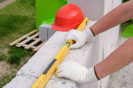 Builders hands in a glove and a building level to check the wall outdoors. New home construction.