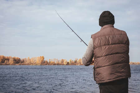 A fisherman with a fishing rod stands on the bank of the river and catches fish. Fisherman on an...