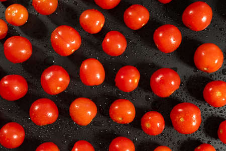 Top shot of fresh cherry tomatoes with water drops on kitchen black tableの写真素材