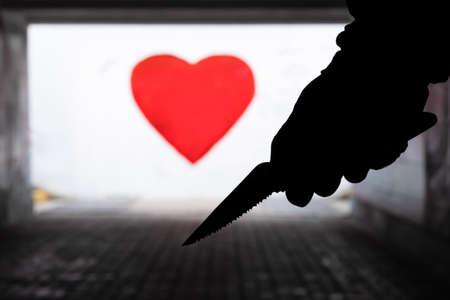 Silhouette of a man with a knife in his hand against the background of a red heart in an underpass. Unhappy love conceptの写真素材