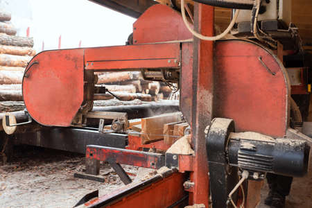 Processing wooden boards at a sawmill. In the process of processing logs on the equipment of the sawmill, a tree trunk is cut into planks. Sawing machine in a wood production plantの写真素材