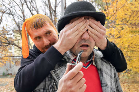 Young man closing his eyes to a man with his hands, making a surprise in the park.の写真素材