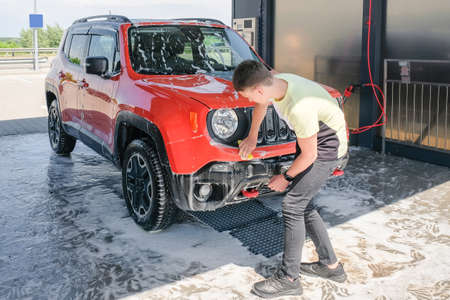 A teenager washes a car with soap at a car wash. Manual car washの写真素材