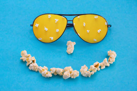Popcorn and glasses in the form of a smile, on a blue background. abstract image. Pastime of the conceptの写真素材