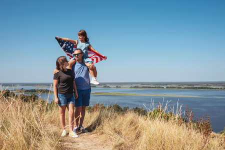Happy family, father, mother and daughter with america flag on natureの写真素材
