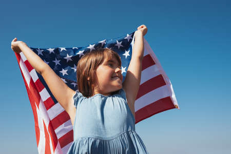 Portrait of a happy girl with the American flag in her hands against the background of the skyの写真素材