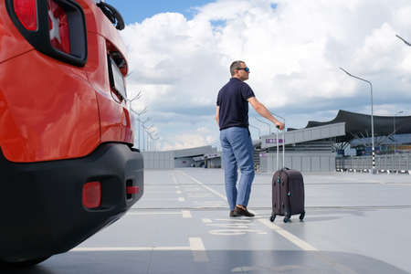 A man with a suitcase in his hands for a trip to the airport car park. View from the back. Travel conceptの写真素材