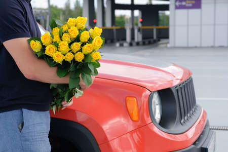 Cropped view of a man with a bouquet of yellow roses and a car in the parking lot. Travel conceptの写真素材