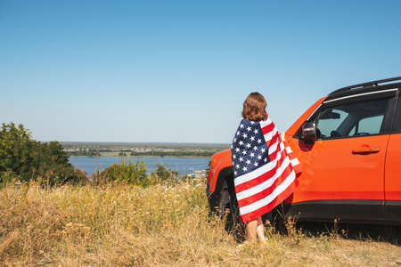 Young woman with USA flag near car enjoying nature.の写真素材