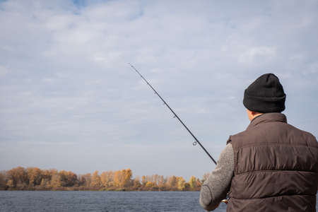 A man with a fishing rod fishing on the background of the river. Fishing relaxation concept