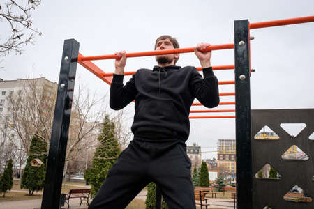 A young man on the playground is doing pull-up exercise at the crossbar. A man is engaged in sports outside, fitness, sport, lifestyleの写真素材