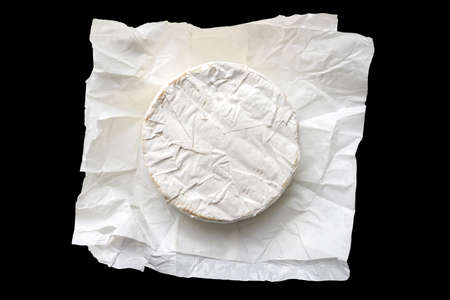 Brie cheese in craft white paper isolated on black background. Camembert cheese top view.の写真素材