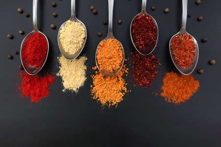 Spoons with spices on a black background. View from above. Colorful spices in spoons