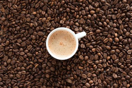 White cup of espresso and roasted coffee beans as a background.