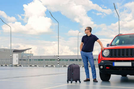 Travel concept. Young businessman standing near his car with luggage in airport parking lot. Business tripの写真素材
