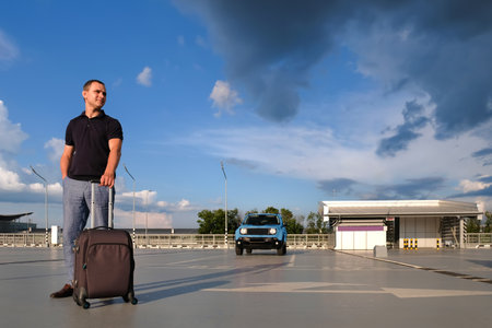 Man in sunglasses and holding a suitcase, in the outdoor parking. Vacation, business trip, vacation conceptの写真素材