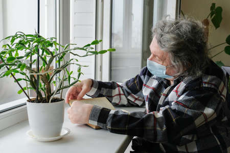An elderly man in a protective mask on self-isolation at home, reads a book. Self-isolation quarantine due to the global coronavirus pandemic. Lifestyleの写真素材