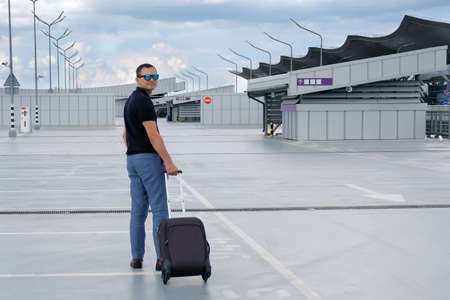 Businessman with a suitcase in an open parking lot at the airport. Business, business trip, travel conceptの写真素材